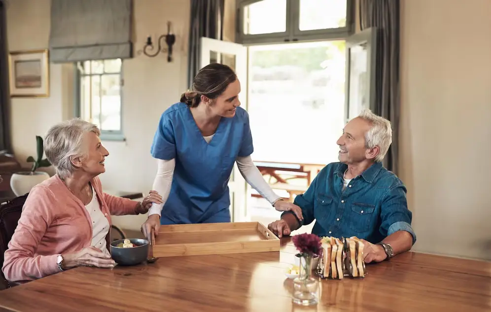 Shot of a young nurse checking up on a senior couple during breakfast at a nursing home Shot of a young nurse checking up on a senior couple during breakfast at a nursing home